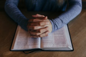 hands folded over an open Bible